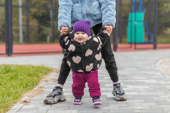 Toddler taking first steps holding older sister's hands