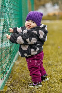 Toddler standing with support holding fence looking back