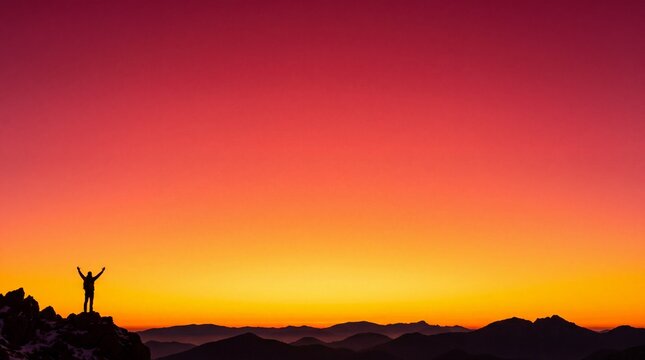 Hiker with raised arms on a mountain peak at sunrise, red and gold sky background