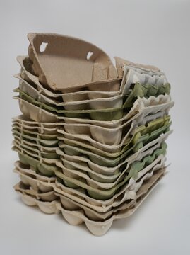 Stack of empty cardboard egg cartons in beige and green colors. Piled up on a white background. Packaging, recycling, and food storage concept.