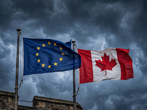 official flags of european union and canada waving against dark stormy sky and stone wall background symbolizing international alliance diplomatic relations and partnership