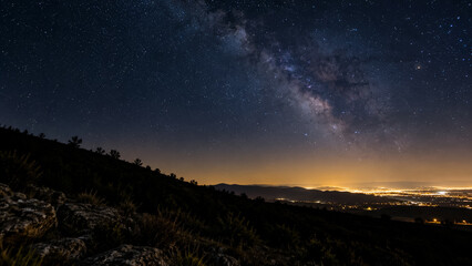 Fototapeta premium Milky Way galaxy over night landscape with distant glowing city lights on horizon. Concept of starry sky, astrophotography, stars, night sky. Copy space.