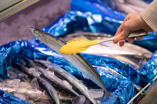 スーパーの鮮魚売り場でトングを使って新鮮なサンマ（秋刀魚）を選ぶ買い物客の手元
