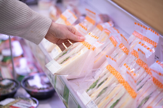 スーパーやコンビニの売り場でランチのサンドイッチを選ぶ買い物客の手元
