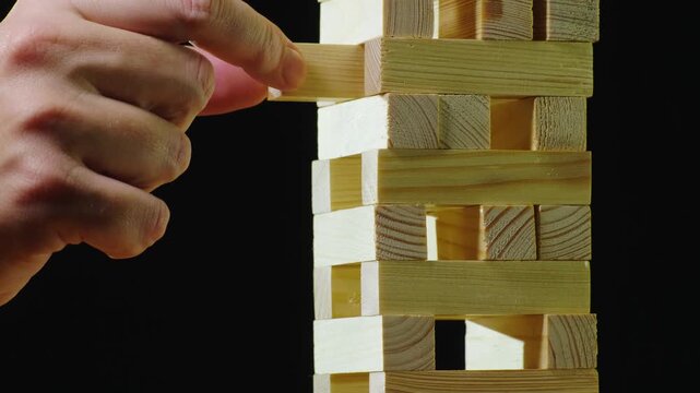 Close up slow motion of hand pulling out wooden block from tower construction, playing jenga game.