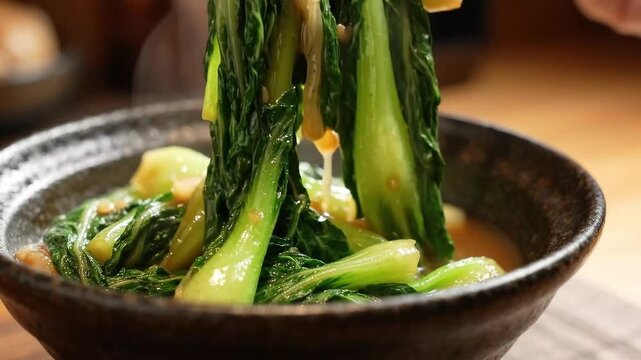 Chopsticks Lifting Fresh Stir-Fried Bok Choy from Ceramic Bowl