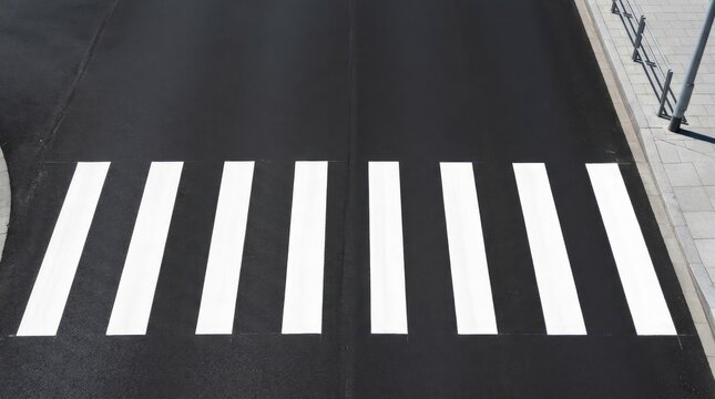 A black crosswalk is prominently displayed on a wet asphalt surface. White stripes delineate the pedestrian crossing.