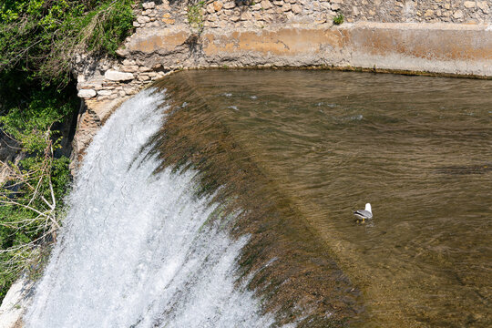 Water cascades over a weir beside a stone wall