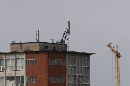 Cellular antennas on the roof of an ageing brick and concrete building beside a yellow tower crane in Bucharest