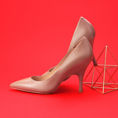Chic women's footwear emphasizing form and color contrast. The neutral leather pumps and metallic gold prop are set against a passionate red backdrop, highlighting modern design and striking visual © Maryna