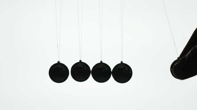Newtons cradle demonstration showing kinetic energy transfer and momentum physics in studio silhouette.