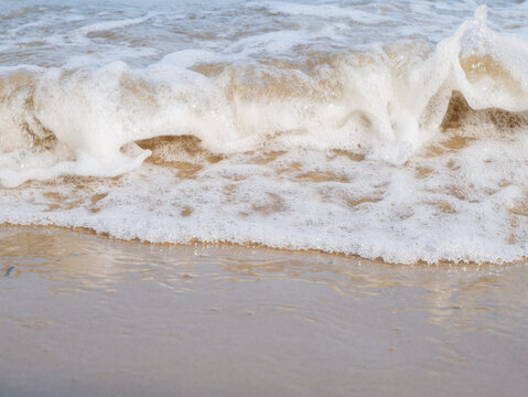 Ocean wave splashing white foam on wet sandy beach shoreline close up