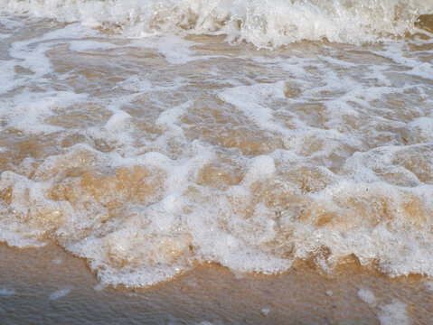 Ocean wave splashing white foam on wet sandy beach shoreline close up