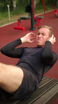 Man training abs on a bench on an outdoor fitness bench. Young man performing abdominal crunches on a bench at an outside gym. Intense bodyweight workout at a street gym.