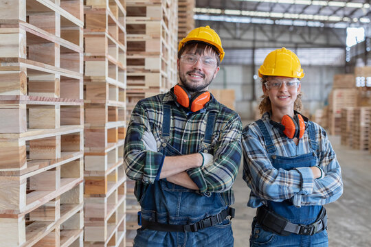 Workers stand in a warehouse filled with wooden pallets while wearing safety gear and smiling at the camera