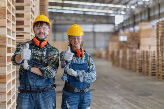 Workers stand in a warehouse filled with wooden pallets while wearing safety gear and smiling at the camera