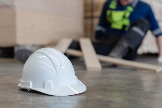 Close-up on white hard hat with blurred injured factory worker on the floor