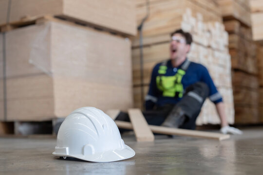 Close-up on white hard hat with blurred injured factory worker on the floor