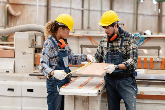 Worker measures wood in a warehouse during the day while wearing safety gear