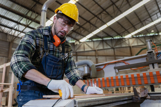Worker measures wood in a warehouse during the day while wearing safety gear