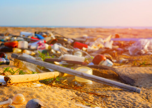 Plastic trash and debris scattered across sandy beach at sunset, environmental pollution concept with warm golden light and shallow depth of field