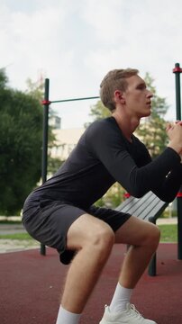 Young man doing squats at an outdoor gym. Athletic man training leg muscles and glutes with classic squats during. Man doing a fitness workout outside. Athlete doing deep bodyweight squat on leg day.