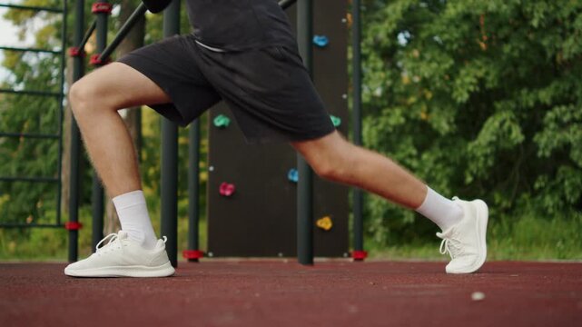 Athlete in black sportswear performing a deep lunge on an outdoor gym. Man doing leg training outside. Athletic man doing a lower body lunge workout. Leg day.