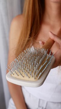 Close-up of woman showing hairbrush full of fallen hair, excessive hair loss and shedding problem