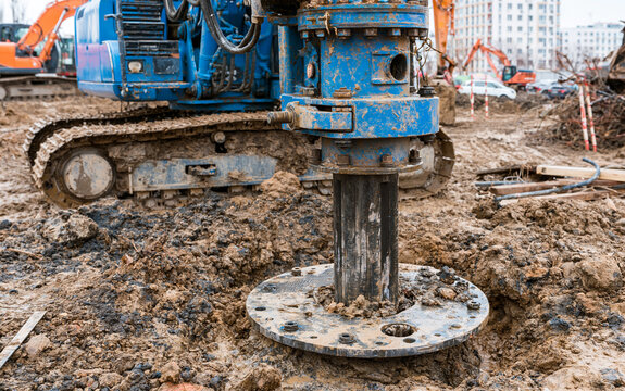 Heavy drilling machine excavating deep circular hole in muddy ground with construction equipment operating for foundation and infrastructure work
