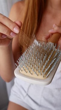 Close-up of woman removing fallen hair from hairbrush showing excessive hair loss and shedding problem