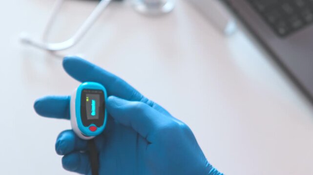 Doctor in blue gloves using a portable pulse oximeter to check oxygen level and pulse rate