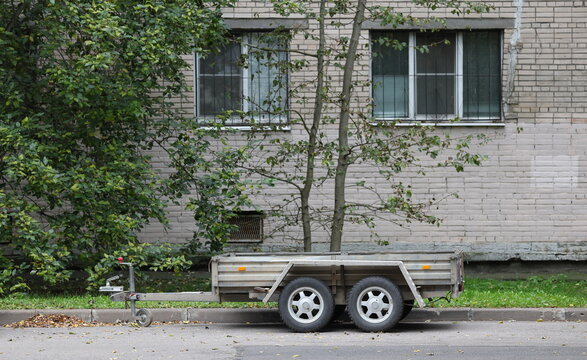 An open four‑wheeled trailer for a passenger car has been left under the windows of a residential building