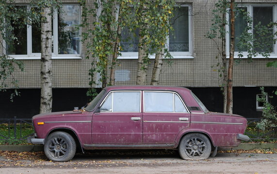An old cherry‑colored car is parked under the windows of a residential building