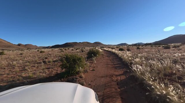 A white car is driving along a narrow, bumpy road with a poor surface in the African savanna.