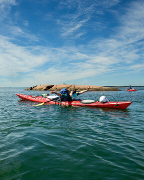 Vertical view of sea kayaker stretching arms wide while leaning back on red kayak, sky copy space above, Georgian Bay, Ontario