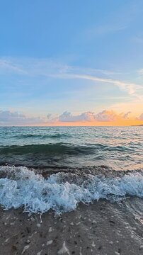 Vertical slow motion footage of a walk parallel to the shoreline at sunset, capturing waves breaking on the beach and warm golden evening light in Sardinia.