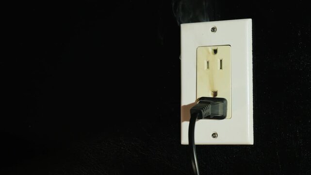 Electrical socket with a plug sparks and emits smoke indicating danger of fire hazard.