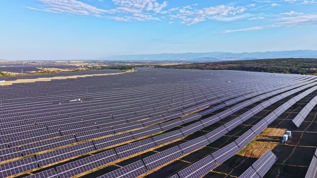 A large field covered in solar panels spread across the landscape. The area has mountains in the background and a bright blue sky.