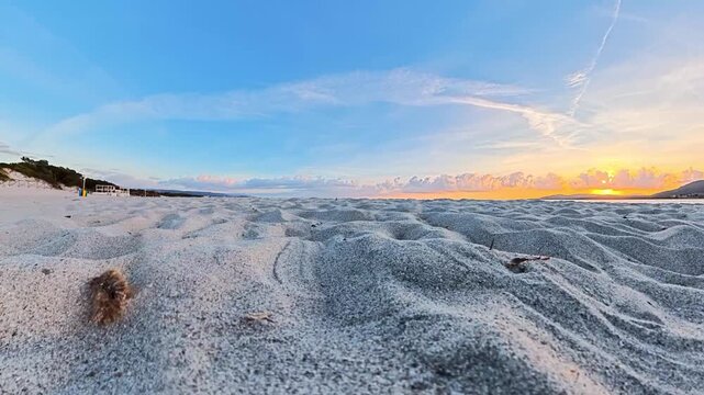 Very low POV camera movement almost touching the sand while walking toward the sea at sunset, continuing along the beach until reaching the shoreline and water.