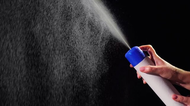 Woman hand spraying air freshener from white aerosol can on black background in slow motion.