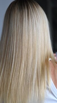 Hair after keratin straightening treatment. Close up shot of a girl&rsquo;s straight blonde hair with dark roots. Woman with smooth blonde hair after a haircut in a beauty salon.
