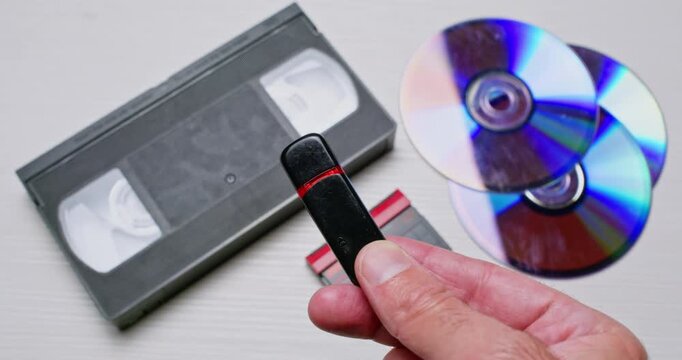 A person holds a USB flash drive against a background of older storage media, removes the cap, and shows the connector.