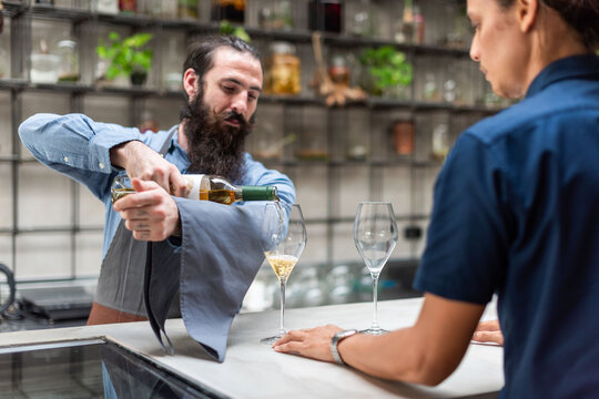 Bartender pouring wine for a customer at a modern bar.