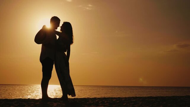 Couple dancing romantically on beach at sunset, silhouette footage.