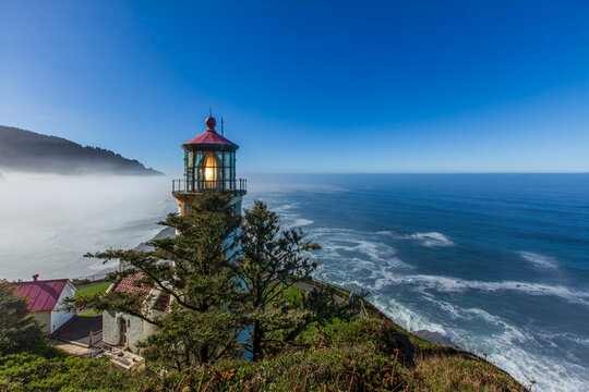 Beautiful scenic view of a historic working lighthouse with a glowing light on a cliff over the ocean at sunrise