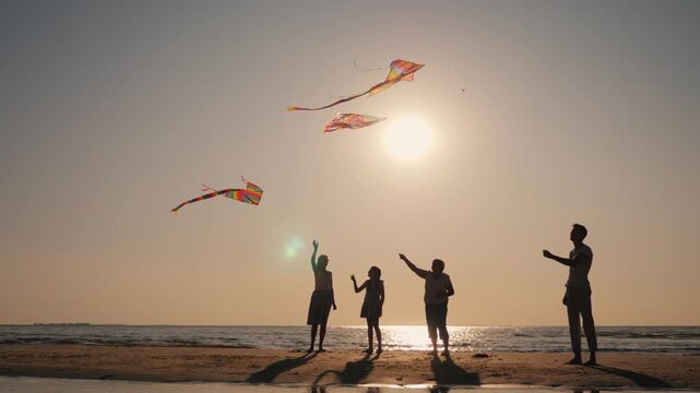 Silhouette of happy family flying kites on beach during sunset time.