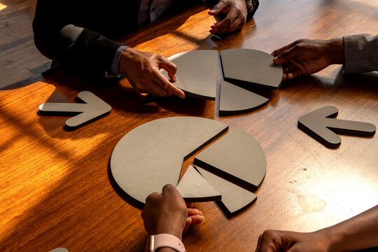 Diverse hands of men and women assembling pie charts around a wooden table