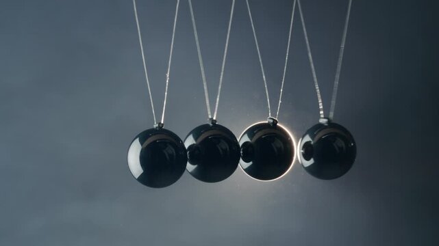 Newtons cradle demonstration showing momentum and energy conservation with black glossy spheres in studio lighting.