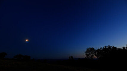 Moon on a twilight sky with stars, planets and landscape mountain silhouettes. © astrosystem