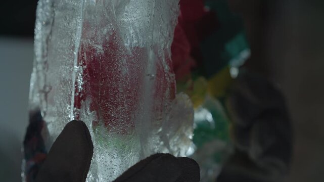 Closeup gloved hand touches icy vial, red residue visible through clear ice, condensation forming on surface, precise thawing technique in controlled lab space, protective glove and suit, radiation